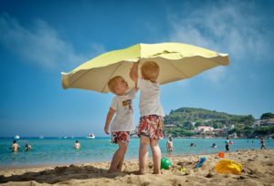 kids under beach umbrella to prevent sunburn
